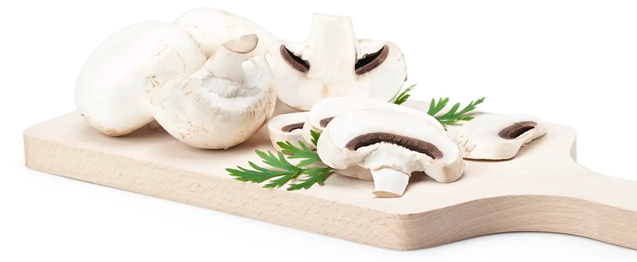 Whole and sliced white mushroom with greens on a wood cutting board